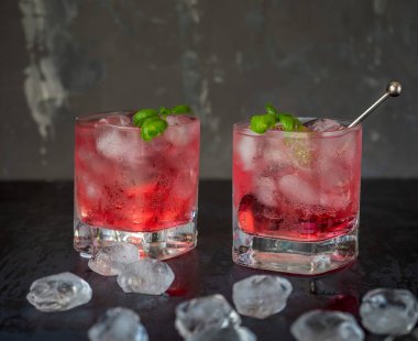 İki bardak bardakta maden suyunda, koyu arkaplanda nane filizi ve buz küpünün yanında vişne suyu serinletiyorum.