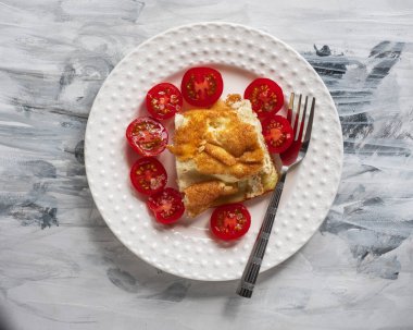 Beyaz tabakta omlet, siyah beyaz peçeteli domatesler ve masa çatalı manzaralı yakın çekim.