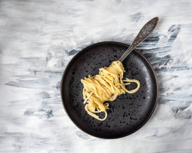 Siyah beyaz kağıt peçeteyle siyah yuvarlak bir tabakta çatala sarılı spagetti tabağı.
