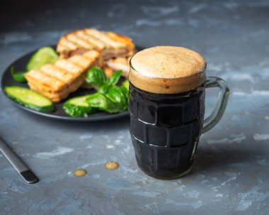 Jambonlu ve peynirli sandviç biralı aperatif, gri arka planda koyu biralı cam bardak.