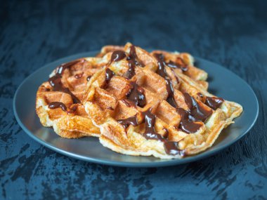 Koyu bir tabakta çikolata kaplı süzme peynirli waffle 'lar yakın plan gri bir arka planda.