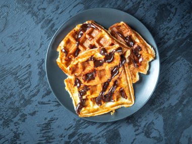 Gri arka planda gri bir tabakta çikolata kaplı üç waffle.