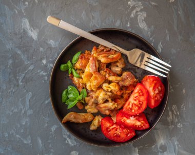 Aperatif ve kızarmış tavuk eti ve koyu bir tabağa serpiştirilmiş kırmızı domates.