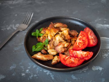 Tavuklu fileto ve doğranmış kırmızı domatesli kahvaltı siyah tabak ve fesleğen yaprakları.