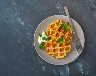 Gri arka planda yuvarlak bir tabakta kremalı mantar sosu ve fesleğen yapraklı sebze kabaklı waffle.
