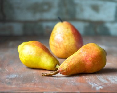 Tahta kahverengi arka planda üç olgun sarı-kırmızı armut.
