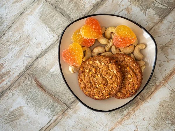 Sweets and nuts on a small rectangular plate, oatmeal cookies and heart-shaped marmalade, top view