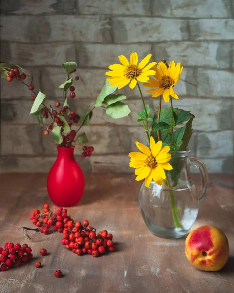 Still life with rowan and rudebequia in a glass and red vase in a rustic kitchen