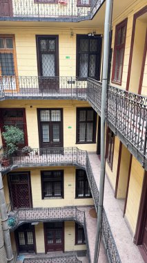 Avrupa avlu manzarası, birden fazla balkon, sarı cephe ve saksı yeşili. Demir parmaklıklı simetrik eski mimari ve retro yerleşim yeri, tipik kentsel konut tasarımı. 