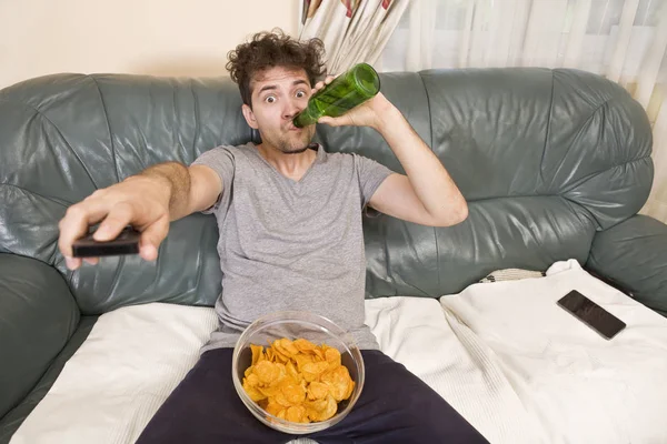 A young man watches television and changes channels while relaxing