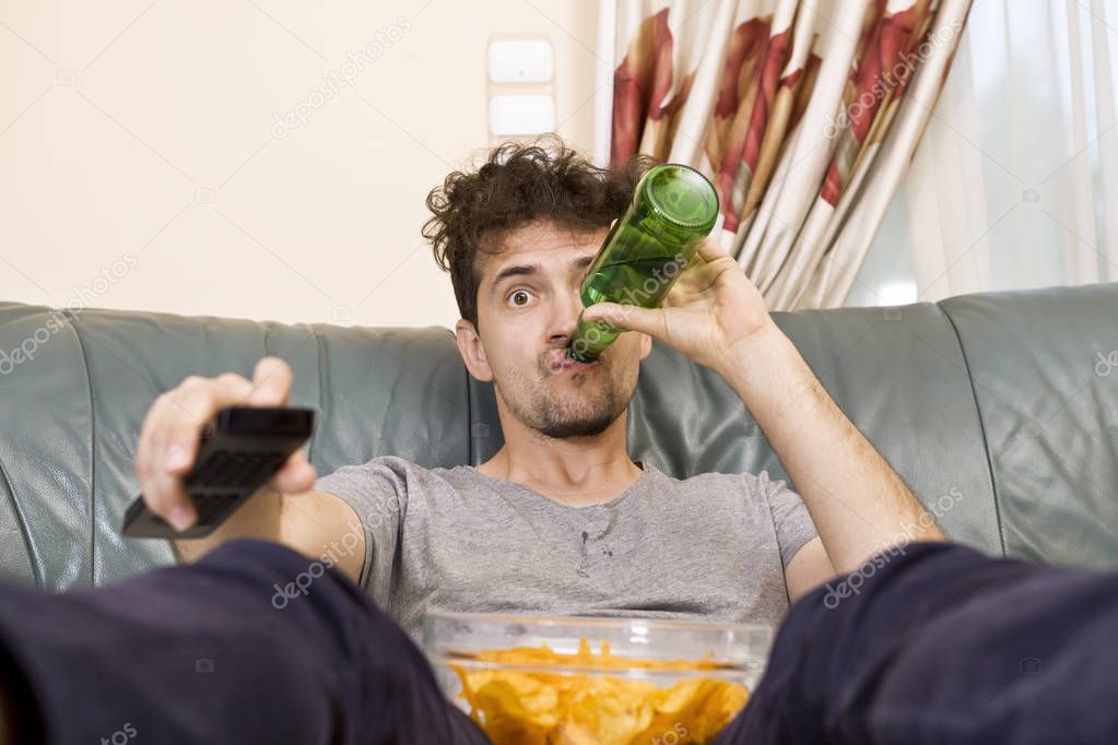 Excited young man with the remote and beer and chips on the couch