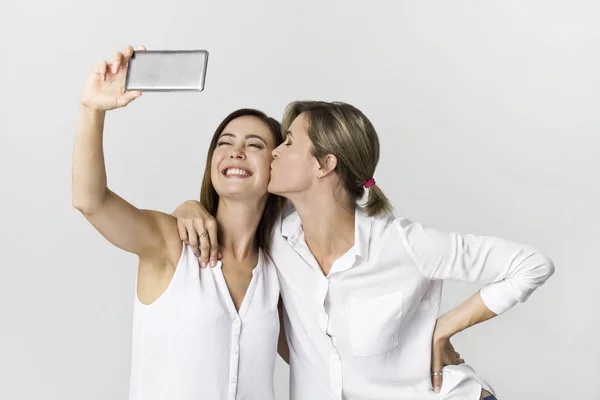 İki genç kadın beyaz gömlekli selfie yapım ile eğleniyor. Beyaz arka plan üzerinde atış stüdyo