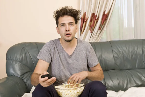 Man with beer and popcorn watching TV at home