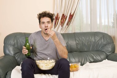 Uzaktan kumandalı ve patlamış mısır tv izlerken kanepede genç adam heyecanlı