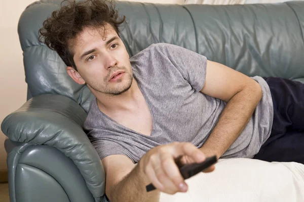 A young man watches television and changes channels while relaxing