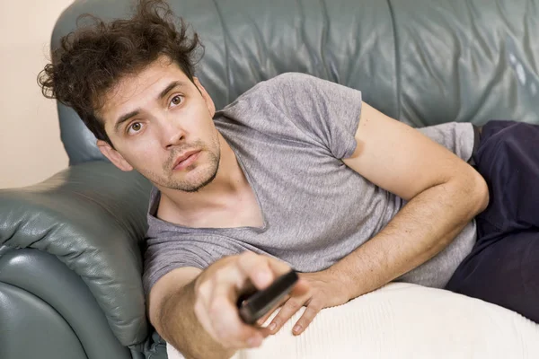 A young man watches television and changes channels while relaxing