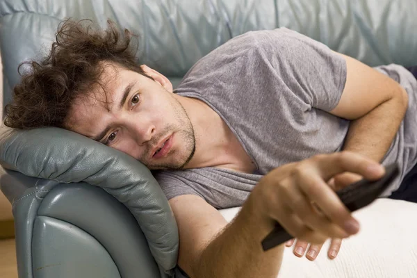 A young man watches television and changes channels while relaxing