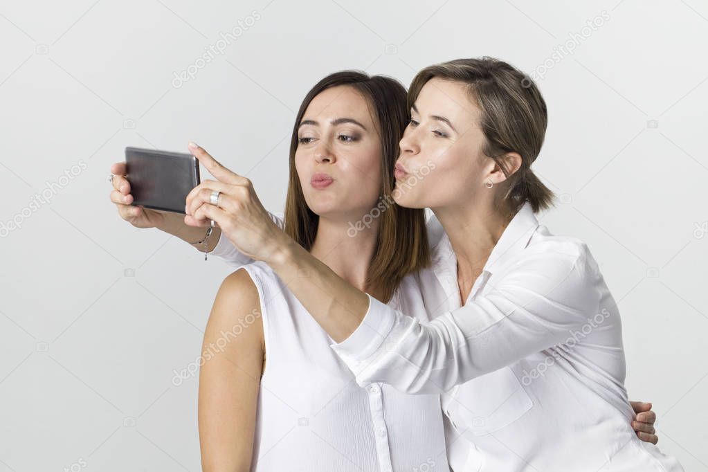 Happiness two young adult model making selfie and send air kiss in screen smart phone against white background
