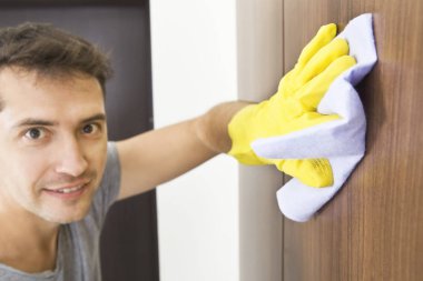 Temizlik hizmeti. Bez ve apartman dairesinde sarı koruyucu eldivenler ile genç adam temizler