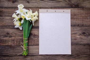 Bir parça kağıt bir ahşap rustik arka plan üzerinde planlama ve güzel hassas nergis çiçek bir buket