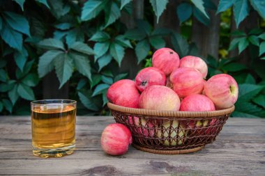 Lezzetli elma suyu bir cam ve ahşap rustik arka plan üzerinde bir hasır tabak içinde güzel kırmızı elmalar