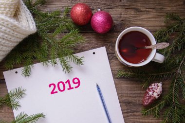 Güzel Noel resim düzeni kartpostal 2019 yeni yıl ile: bir bardak çay, bir defter bir kalem için planları, çam dalları ile oyuncaklar, ahşap rustik arka plan, sıcak bir eşarp ile ana sayfa görünümü