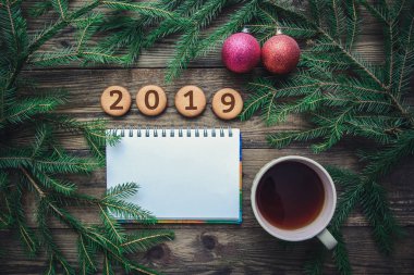 2019 yılbaşı kurabiye, çam dalları, oyuncak, sıcak eşarp ve bir fincan sıcak çay ahşap arka plan üzerinde renkli Noel resimle