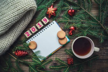 2019 yılbaşı kurabiye, çam dalları, oyuncak, sıcak eşarp ve bir fincan sıcak çay ahşap arka plan üzerinde renkli Noel resimle