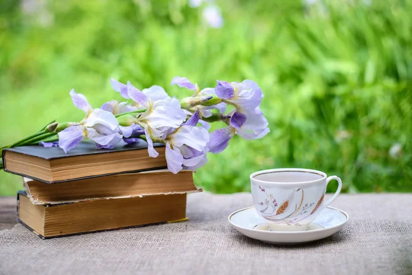 Une pile de vieux livres, des iris violets et une tasse de thé — Photo