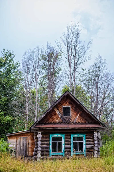 Vecchia casa in legno sullo sfondo di alberi nudi e cielo nuvoloso — Foto Stock