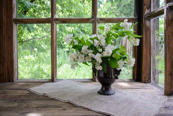 A beautiful bouquet of Jasmine branches in a vase by a wooden window in the countryside