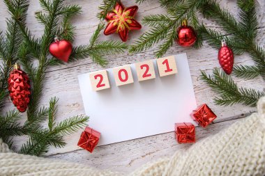 2021 yılı. Beyaz ahşap arka planda yeşil dalları ve kırmızı cam oyuncakları olan şenlikli yeni yıl arkaplanı, kopyalama alanı