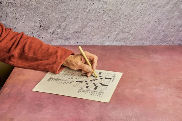 Masada elinde kalemle bulmaca çözen bir yetişkin. Yakın plan, boşluğu kopyala.