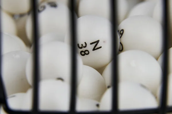 Bingo piyango topu dağıtıcısı, siyah metal örgü ve krank kolundan yapılmış. Önplanda beyaz arkaplan.