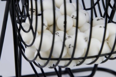 Bingo piyango topu dağıtıcısı, siyah metal örgü ve krank kolundan yapılmış. Önplanda beyaz arkaplan.