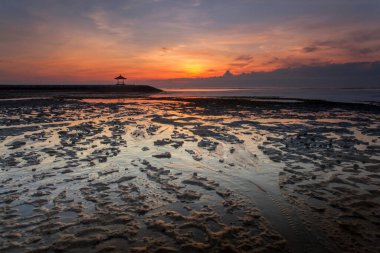 Sanur, Endonezya 'nın Bali adasının güneydoğusunda bir sahil kasabasıdır. Kumsalın uzun uzantısı sığ suları sunuyor. Kumda renkli jukung balıkçı tekneleri dinleniyor.,