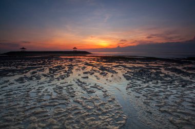Sanur, Endonezya 'nın Bali adasının güneydoğusunda bir sahil kasabasıdır. Kumsalın uzun uzantısı sığ suları sunuyor. Kumda renkli jukung balıkçı tekneleri dinleniyor.,