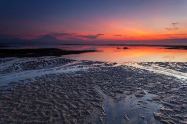 Sanur, Endonezya 'nın Bali adasının güneydoğusunda bir sahil kasabasıdır. Kumsalın uzun uzantısı sığ suları sunuyor. Kumda renkli jukung balıkçı tekneleri dinleniyor.,