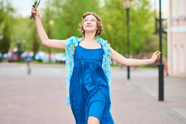 Bella ragazza-artista per strada con un vestito blu, sorridente, con le nappe in mano — Foto Stock