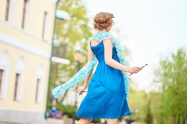 Bella artista ragazza per strada in abito blu, con nappa in mano dal retro — Foto Stock