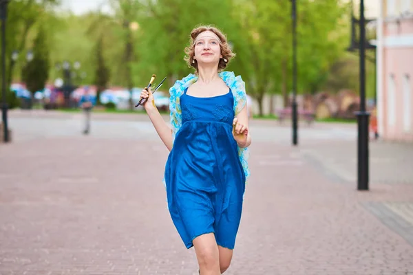 Belle fille-artiste dans la rue en robe bleue, souriante, avec des glands dans les mains — Photo
