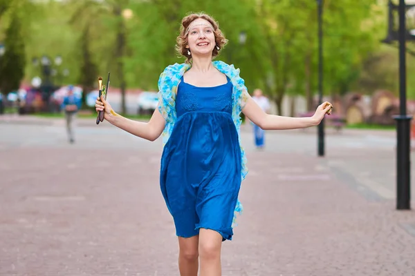 Schöne Künstlerin auf der Straße in einem blauen Kleid, lächelnd, mit Quasten in den Händen — Stockfoto