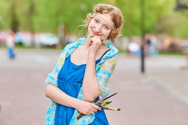 Schöne Künstlerin auf der Straße in einem blauen Kleid, lächelnd, mit Quasten in den Händen — Stockfoto