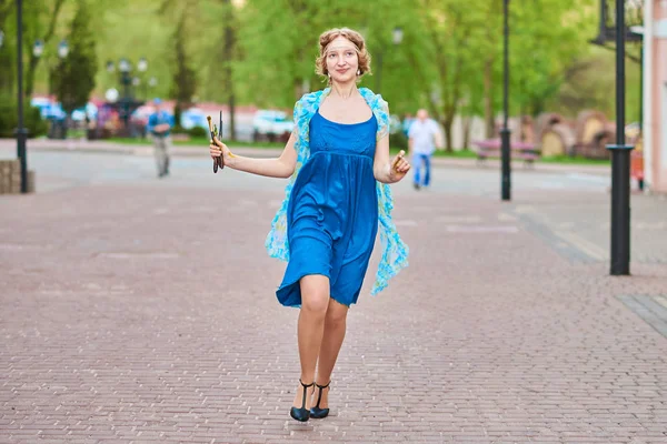 Bella ragazza-artista per strada con un vestito blu, sorridente, con le nappe in mano — Foto Stock