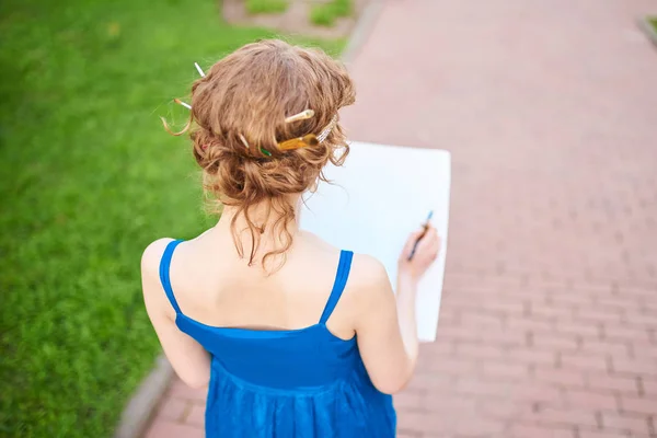 Schöne Künstlerin auf der Straße in einem blauen Kleid zeichnet eine Skizze des Bildes — Stockfoto