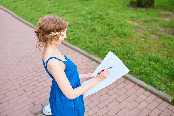Mooi meisje-artiest op de straat in een blauwe jurk tekent u een schets van de afbeelding — Stockfoto
