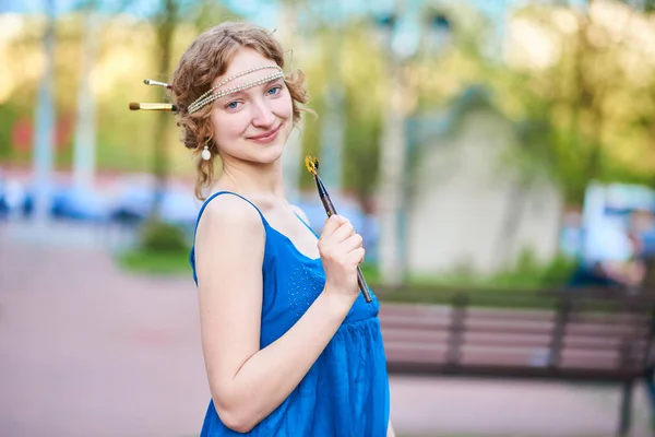 Linda menina-artista na rua em um vestido azul, sorrindo, com borlas em suas mãos — Fotografia de Stock