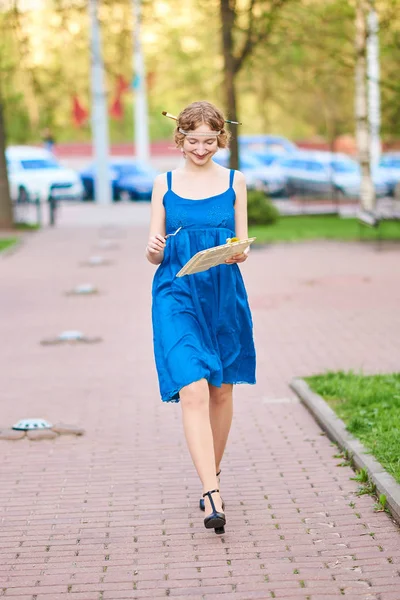 Vacker flicka-artist på gatan i en blå klänning, leende, med tofsar och palett i hennes händer — Stockfoto