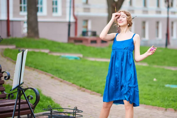 Belle fille-artiste dans la rue en robe bleue, souriante, avec des glands dans les mains — Photo