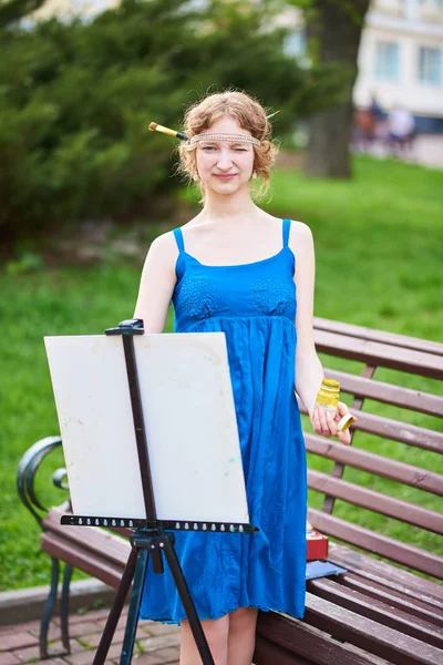 Linda menina-artista na rua em um vestido azul, desenha no cavalete — Fotografia de Stock